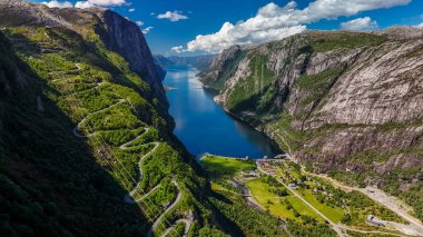 Norveç 'in yemyeşil dağlarının arasından süzülen dolambaçlı bir yolun havadan görünüşü. Uzakta uzanan koyu mavi bir fiyort. Kjerag, Lysebotn, Lysefjorden, Norveç