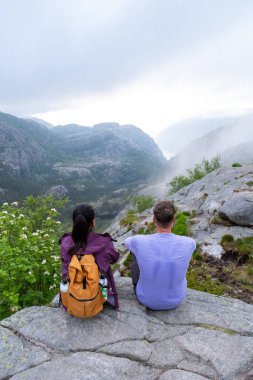 Baş döndürücü Norveç fiyorduna bakan kayalık bir uçurumda oturan iki kişi nefes kesen manzaranın ve barışçıl atmosferin tadını çıkarıyorlar. Norveç, Preikestolen 'de yürüyüş yapan bir çift.