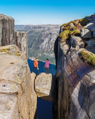 Norveç 'te Kjeragbolten Minber Kayası' nın kenarında duran iki kişi aşağıdaki nefes kesen vadiye bakıyor. Kjeragbolten Norveç 'i ziyaret eden birkaç erkek ve kadın