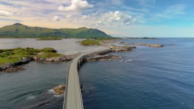 Nefes kesici bir hava perspektifi, sakin bir su kütlesi üzerinde uzanan ve bölgedeki muhteşem doğal manzarayı vurgulayan bir köprüyü ortaya çıkarıyor. Atlantik Okyanusu Yolu, Atlanterhavsveien, Norveç