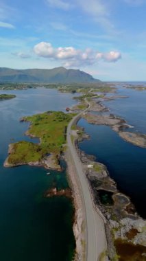Berrak bir gökyüzü altında sakin bir su kütlesini kesen bir yolun manzaralı görüntüsü Atlantik Okyanus Yolu, Atlanterhavsveien, Norveç manzarasının doğal güzelliğini yakalıyor.