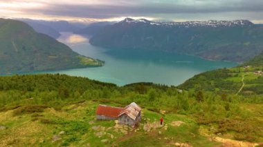 Molden, Norveç 'ten LustraFjord, dağlarla çevrili, göle bakan bir tepede küçük bir ev ve kulübe. Sahne yeşil ağaçlar ve sakin bir göl içeriyor, resim gibi bir manzara yaratıyor.