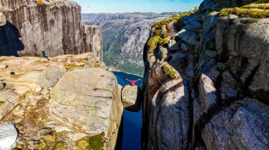 Norveç 'te Kürsü Kayası olarak da bilinen Kjeragbolten' in kıyısında oturan bir yürüyüşçü derin bir vadiye ve çarpıcı bir fiyort manzarasına bakıyor..