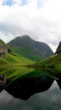 Huzurlu görüntü, sakin bir gölde yansıtılan, sisli tepelerle çevrili yeşil bir dağı yakalıyor, Urke Norveç.