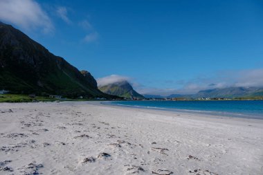 Norveç 'te arka planda dağlar ve ön planda sakin bir okyanus olan beyaz bir kumsal manzarası. Kumsal boş görünüyor, Ramberg Plajı Lofoten Norveç