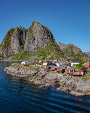 Norveç 'te küçük bir köyün manzaralı manzarası, yüksek dağların altındaki kayalık kıyı şeridine yerleşmiş kırmızı kulübeler. Lofoten Adaları 'ndaki Hamnoy balıkçı köyü, Norveç' te kırmızı rorbu evleri var.
