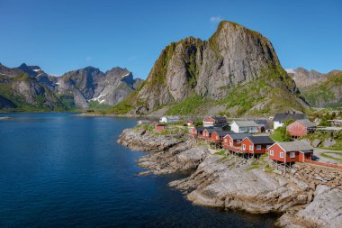 Norveç 'te bir fiyordun kayalık kıyısına tünemiş kırmızı kulübeler, yüksek dağlar ve açık mavi gökyüzü ile çevrili. Lofoten Adaları 'ndaki Hamnoy balıkçı köyü, Norveç' te kırmızı rorbu evleri var.