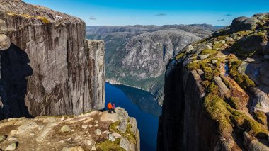 Norveç 'teki Kjeragbolten uçurumunun kenarında duran iki birey fiyort ve etrafındaki dağların nefes kesici manzarasına bakıyor. Norveç, Kjeragbolten 'i ziyaret eden iki erkek ve kadın