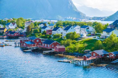 Norveç 'in büyüleyici kıyı kasabasının panoramik bir görüntüsü. Rıhtım boyunca demirlerin üzerine renkli kırmızı kulübeler inşa edilmiş. Reine, Lofoten, Norveç