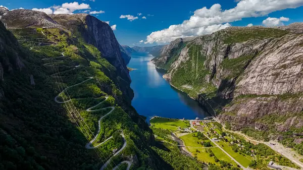 Güzel güneşli bir günde Norveç 'te sakin bir fiyorda bakan yemyeşil dağların arasından kıvrılarak geçen dolambaçlı bir yolun hava manzarası. Kjerag, Lysebotn, Lysefjorden, Norveç