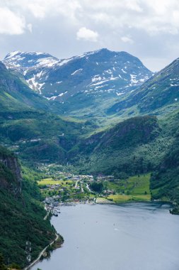 Norveç fiyort vadisinin göz kamaştırıcı hava manzarası, karla kaplı dağlar, yemyeşil bitki örtüsü ve pitoresk bir köye uzanan dolambaçlı bir nehir. Norveç 'in Geiranger' si