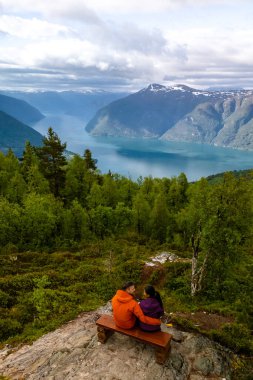 Bir çift Norveç 'te yemyeşil ve nefes kesici dağ manzaralarıyla çevrili çarpıcı bir fiyorda bakan bir bankta oturuyor. Molden yürüyüşü, Norveç