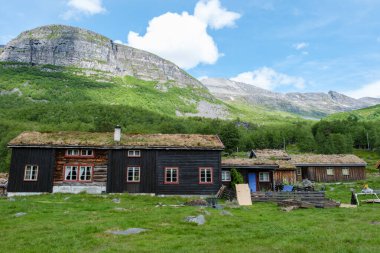 Çimen çatılı geleneksel bir Norveç kulübesi yemyeşil bir dağ manzarasının ortasında yer alır. Innerdalen Vadisi Norveç