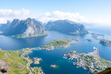 Dramatik dağların ve kristal berrak suların arasına kurulmuş büyüleyici bir kıyı köyünü gösteren pitoresk bir Norveç fiyordunun hava görüntüsü. Reinebringen, Lofoten, Norveç
