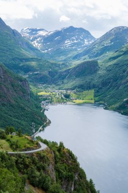 Norveç 'in yemyeşil dağlarında kıvrılarak ilerleyen, pitoresk bir fiyorda bakan dolambaçlı bir yolun manzarası. Norveç 'in Geiranger' si