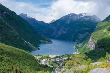 Yeşil dağlarla çevrili bir Norveç fiyordunun manzarası. Su sakin ve mavidir ve gökyüzü temizdir. Norveç 'in Geiranger' si
