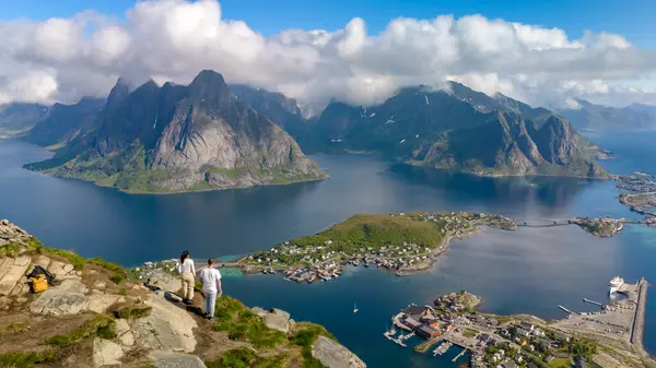 stock image A stunning panoramic view of the Lofoten Islands in Norway, showcasing the rugged mountains, deep fjords, and charming villages. Two people stand on a cliff overlooking the Reinebringen Lofoten Norway