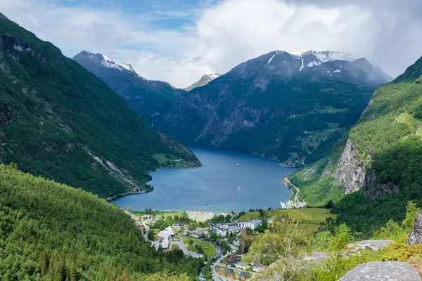 Yeşil dağlarla çevrili bir Norveç fiyordunun manzarası. Su sakin ve mavidir ve gökyüzü temizdir. Norveç 'in Geiranger' si