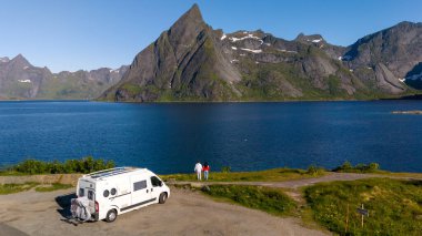 Norveç 'te pitoresk bir fiyortun yanına beyaz bir karavan park edilmiş. Bir çift de göz kamaştırıcı dağ manzarasına hayran. Lofoten Norveç