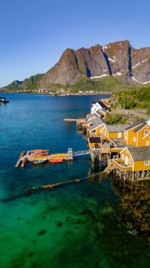 Lofoten kıyısında bulunan ve kristal berrak suya tepeden bakan cambaz kuleleri üzerine renkli evler inşa edilmiş antika bir Norveç köyünün hava manzarası. Sakrisoy, Lofoten, Norveç