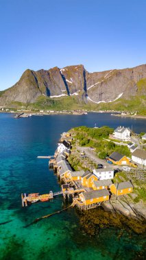 Norveç 'te küçük bir köyün havadan görünüşü, berrak mavi suların üzerine sazlıklar üzerine renkli evler yapılmış. Arka plandaki dağlar dramatik bir zemin sağlıyor. Sakrisoy, Lofoten, Norveç