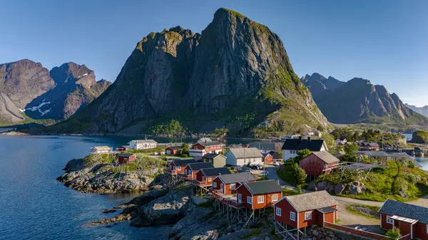 stock image A picturesque view of a small village in Norway, featuring red cabins nestled among rugged mountains and a calm blue fjord. Hamnoy Lofoten Norway