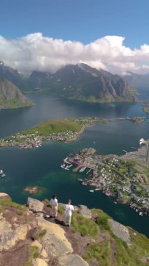 Reinebringen Lofoten Adaları 'nın tepesinde, Reinebringen' in tepesinde duran bir çift kadın ve erkek. Reine bakış açısına giden turistik yol, Reine, Lofoten, Norveç yazın
