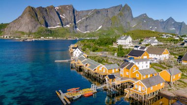 Norveç 'in Lofoten Adaları' ndaki görkemli dağları olan pitoresk bir köyde, ayaklıklar üzerindeki renkli ahşap evlerin hava manzarası. Sakrisoy, Lofoten, Norveç