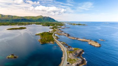 Norveç 'te yeşil yemyeşil adalar ve kristal berrak mavi suları ile pitoresk bir takımadanın içinden geçen dolambaçlı bir yolun havadan görünüşü. Atlantik Okyanusu Yolu Norveç