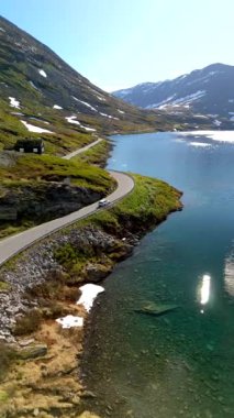 Dağlarla çevrili güzel, berrak bir göl kenarında dolambaçlı bir yol. Kar hala tepeleri kaplıyor. Langvatnet, Geiranger, Norveç