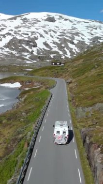 Karlı zirveleri ve huzurlu gökyüzü olan bir dağ yolunda yolculuk yapan bir karavan Langvatnet, Geiranger ve Norveç 'e huzurlu bir sürüş sağlar.