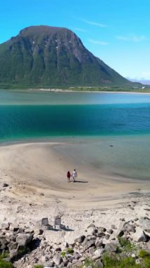 Bir çift, Norveç 'in Lofoten şehrinde karavanı olan dağlarla çevrili güzel bir kumsalın keyfini çıkarıyor.