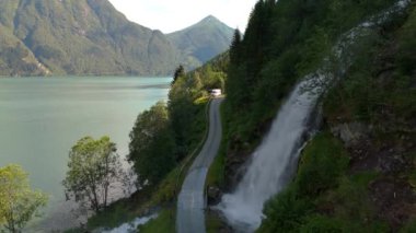 Bereketli yeşilliklerle çevrili, çağlayan şelalesi olan sakin bir göl kıyısında resim gibi bir dağ yolu. Fjaerlandsfjorden, Fjord, Vestland, Norveç
