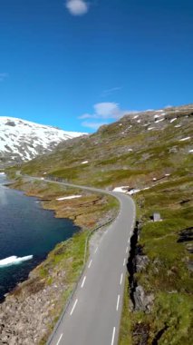 Hava perspektifi, berrak bir gökyüzünün altında dingin bir göl kenarında kıvrılan bir dağ yolunun nefes kesici bir görüntüsünü yakalar. Langvatnet, Geiranger, Norveç