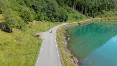 Yeşilliklerle çevrili görkemli göl yolu boyunca giden bir bisikletlinin çarpıcı hava görüntüsü. Lovatnet, Norveç