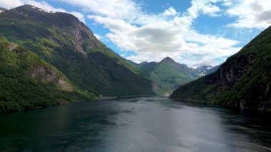Parçalı bulutlu bir gökyüzünün altında görkemli dağlarla çevrili sakin bir fiyort. Doğa ve seyahat içeriği için mükemmel. Geiranger, Norveç
