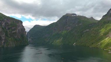 Uzaklarda şelalesi olan yüksek dağlarla çevrili sakin bir fiyordun nefes kesici manzarası. Geiranger, Norveç