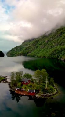 Dağlarla çevrili, gölde kırmızı bir evi olan küçük bir adanın havadan görünüşü. Lovrafjorden, Norveç 'te günlük yaşamdan huzurlu bir kaçış sunuyor.