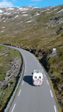 Çimenli tepeler ve açık mavi gökyüzünün altındaki karlı tepelerle çevrili dolambaçlı bir dağ yolunda bir karavan. Langvatnet, Geiranger, Norveç 'te virajlı bir yoldaki minibüs.