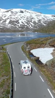 Bir karavan manzaralı gölü ve arka planda karlı zirveleri olan pitoresk bir dağ yolu boyunca seyahat eder. Langvatnet, Geiranger, Norveç