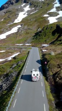 Tepelerde kalan kar parçalarıyla manzaralı bir dağ yolunda giden bir karavanın hava görüntüsü. Langvatnet, Geiranger, Norveç