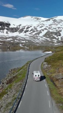 Karavana binip karla kaplı tepeleri ve dingin bir göl manzarası olan dolambaçlı dağ yolları boyunca ilerleyin. Langvatnet, Geiranger, Norveç