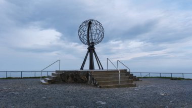 Norveç 'in dramatik manzarasına tepeden bakan bir dizi beton basamağın üzerinde çelik bir küre heykeli duruyor. Nordkapp, Kuzey Burnu