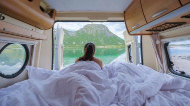 Bir kadın karavanında uyanıyor, Norveç 'teki manzaralı bir dağ gölüne bakıyor. Lofoten Norveç