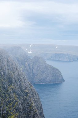 Uçsuz bucaksız okyanus ve engebeli kayalıkların panoramik görüntüsü sisli bir sisle örtülmüş, nefes kesici ve sakin bir manzara yaratıyor. Nordkapp, Kuzey Burnu