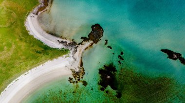 Turkuaz sulara doğru kıvrılan kumlu bir sahil manzarası, yemyeşil çimenler ve kayalık körfezler tarafından çerçevelenmiş. Kolbedeliden Sahili 'nin en üst manzarası, Lofoten.