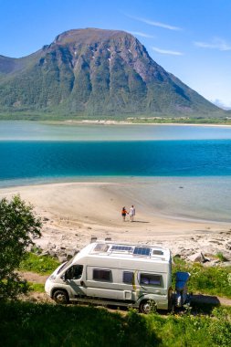 Bir çift el ele yürür el ele el ele el ele, yakınlarda park etmiş bir karavan, muhteşem bir fiyort ve dağ zeminiyle. Lofoten Norveç sahilindeki karavanda.