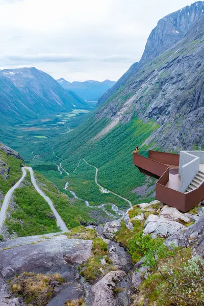 stock image A person stands on a scenic viewpoint overlooking a winding road and a valley in Norway. Trollstigen Road Norway