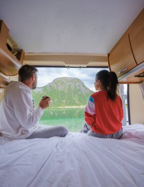 Bir çift, karavanın konforundan huzurlu bir Norveç fiyortunun keyfini çıkarıyor. Lofoten Norveç sahilinin penceresinden bakan bir erkek ve kadın bir karavanın yatağında