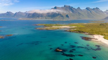 Norveç adasında ıssız bir kumlu sahil kayalık çıkıntıları ve yemyeşil bitkilerle dolu. Turkuaz sular bulutlarla kaplı dağlara çıkar. Kolbedeliden Sahili, Lofoten
